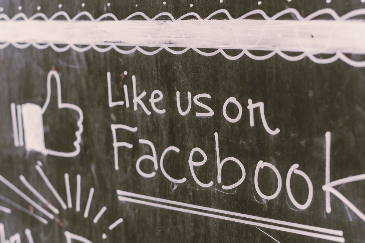 Illustration sur tableau noir encourageant l’engagement sur Facebook avec un message like us.
